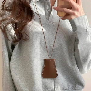 Brown leather trapezoid key case necklace pendant with white stitching on gray sweater