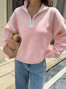 Street style shot of a woman in a pink half-zip knitted sweater in a sunny city setting