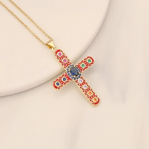 Gold cross necklace with red enamel and colorful zircon stones on marble surface