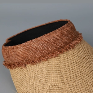 Detailed close-up of straw sun hat featuring brown woven trim and delicate fringe edges