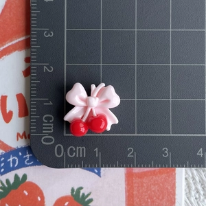 Mini resin cherry charms with pink bow measured on a ruler for scale and size