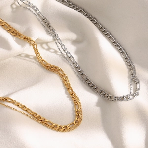 Detail of layered gold and silver stainless steel necklaces on soft white fabric
