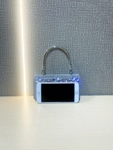 Silver rhinestone handbag with fringe tassels and metal handle beside smartphone for scale