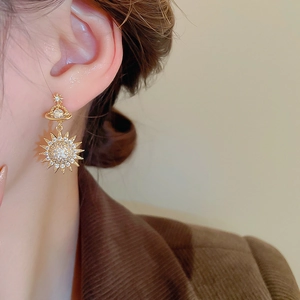 Close-up of elegant gold celestial earrings featuring star and saturn motifs with zircon