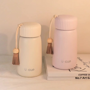 Mini stainless steel insulated water bottles in cream and pink with tassel charms