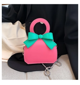 Detail of mini handbag featuring vibrant pink and green bow with silver bead chain strap