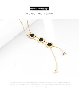 Detail of gold Y-shaped necklace with black round pendants and Roman numerals and zircons
