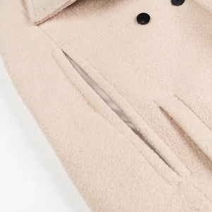 Dettaglio ravvicinato del cappotto in lana crema con texture del tessuto e bottoni neri