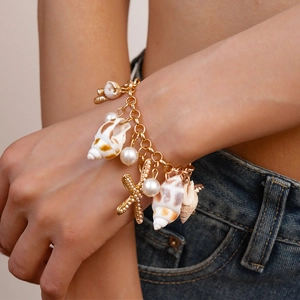 Detail of layered gold bracelet featuring faux pearls, shells and starfish charms on wrist