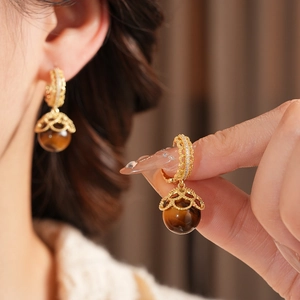 Close-up of gold-plated tiger eye earrings with intricate lace hollow design on a model