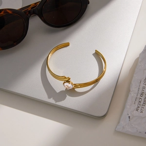Detail of gold-plated open bangle with oval zircon set on a laptop surface