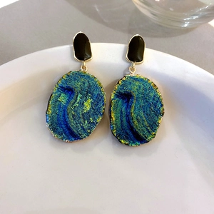 Detail of vintage resin drop earrings with black and iridescent teal pendants on ceramic