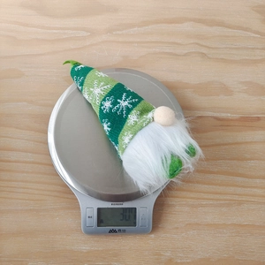 Close-up of a striped knit Christmas gnome toy being weighed on a digital scale