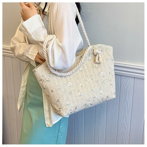 Détail d'un sac cabas tissé crème avec broderie florale et anse en corde à nœuds