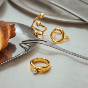 Macro shot of gold pearl rings and geometric bands on a textured fabric background