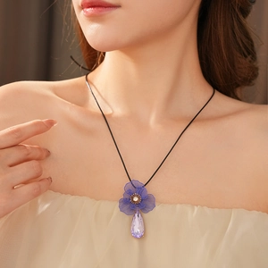 Detailed view of a purple floral pendant with a teardrop crystal on a black cord