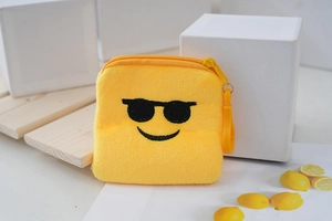Close-up of yellow plush coin purse with black sunglasses smiley face embroidery and hook
