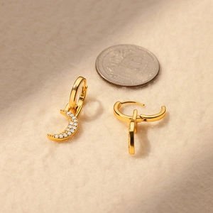 Detail of 18K gold plated crescent moon earrings with cubic zirconia on beige fabric