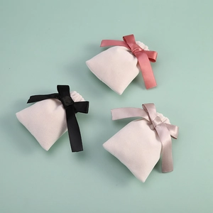 Three elegant beige velvet jewelry pouches with colorful satin ribbon bows on green backdrop