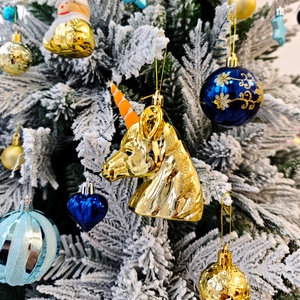 Détail d'une décoration de Noël licorne dorée suspendue à une branche de sapin enneigée