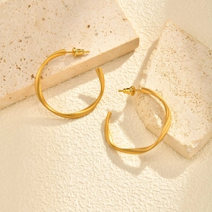 Matte gold C-shaped twisted hoop earrings displayed on a minimalist textured stone background