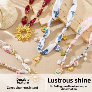 Detailed macro of silk-wrapped gold chain necklaces with enamel floral and pearl charms