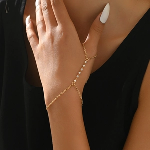Close-up of gold chain finger bracelet featuring white pearls on a model's hand