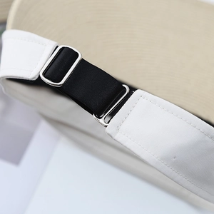 Detail of silver metal buckle and black elastic strap on beige woven sun visor hat