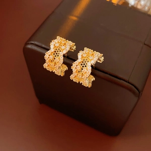 Detailed view of gold-colored honeycomb hoop earrings with pave diamonds on leather