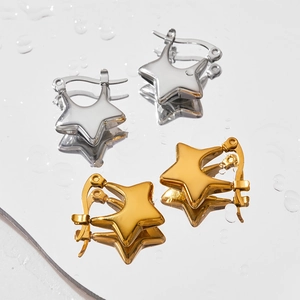 Détail des boucles d'oreilles étoiles dorées et argentées sur une surface d'eau miroir