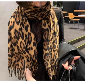 Close-up detail of leopard print scarf with tassels worn by a model in a cozy scene