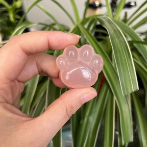 Pink quartz paw carving held in hand with a natural blurred green background