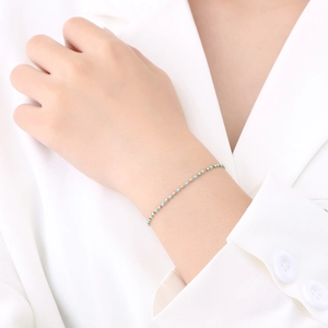Detailed close-up of a slim blue bead and gold metal chain bracelet on a white sleeve