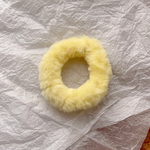 Close-up of a fluffy bright yellow faux fur scrunchie on textured paper background