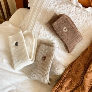 Three pairs of warm winter wool socks with rose embroidery on white pillow background