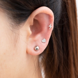 Three minimalist silver stainless steel studs featuring lightning, heart, and ball shapes