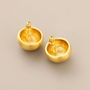 Macro shot of minimalist gold semi-sphere stud earrings with brushed satin metal texture