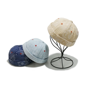 Three paisley brimless caps in navy, light blue and beige on a display stand