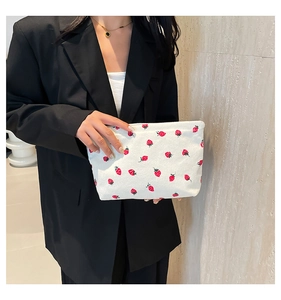 Detail of white corduroy tote bag with red strawberry prints held by a model