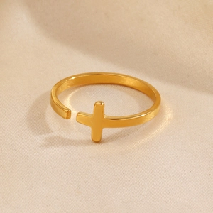 Golden minimalist stainless steel cross open ring shown on a warm textured background