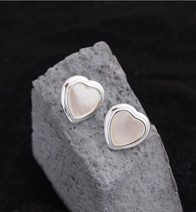 Detailed close-up of heart-shaped silver earrings with mother of pearl inlay on a rock