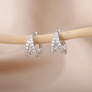 Detailed close-up of silver C-shaped zircon hoop earrings on a minimalist wooden branch
