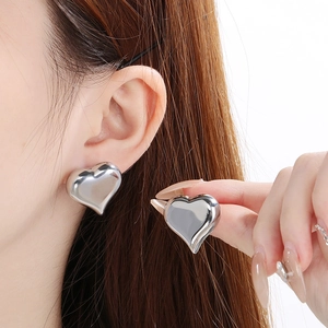 Détail de boucles d'oreilles cœur argentées avec finition polie portées sur un modèle