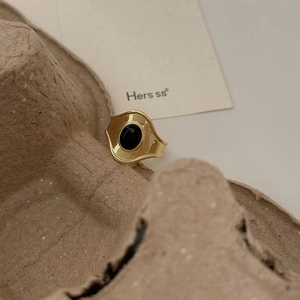 Close-up of a gold wave ring featuring an oval black onyx stone on a textured background