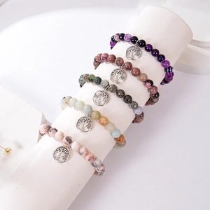 Cinq bracelets variés en pierre naturelle avec pendentif arbre de vie sur support blanc