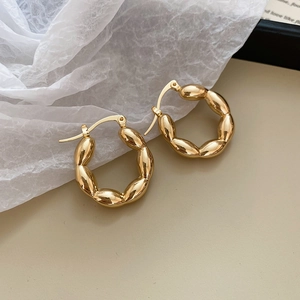 Macro detail of golden twisted croissant hoop earrings with a high-shine metallic finish