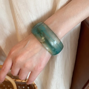 Detail of wide acrylic bangle in teal green showing natural cloudy texture on wrist
