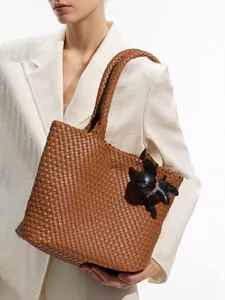 Brown woven leather tote bag with dog charm held by model in white suit