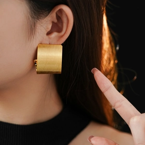 Detail view of gold-plated square brushed metal earrings shown on a model ear