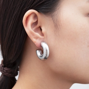 Close-up of a silver hollow round earring with hammered texture worn on a model ear